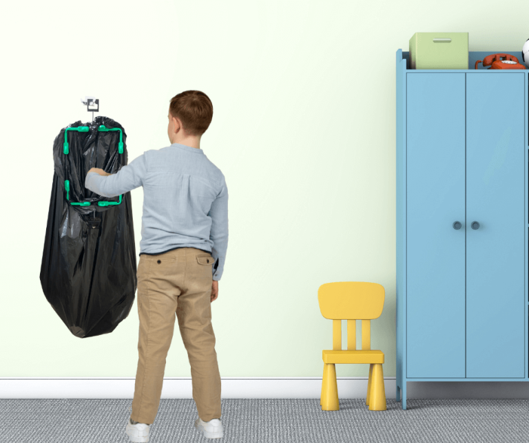 A person is using a wall-mounted trash bag holder with a black bag attached in a room with a blue cabinet and a yellow chair.